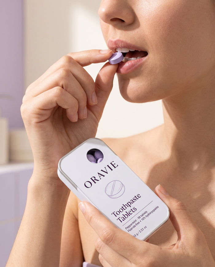 Step 1, chew: woman placing a lavender toothpaste tablet between her lips, holding the ORAVIE tin
