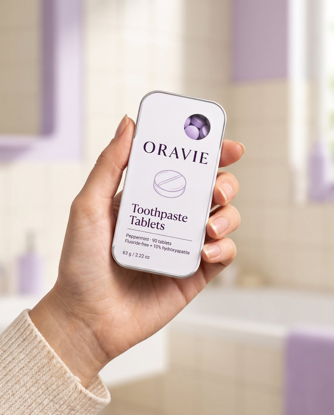 Hand holding the ORAVIE Toothpaste Tablets tin to show its small pocket size