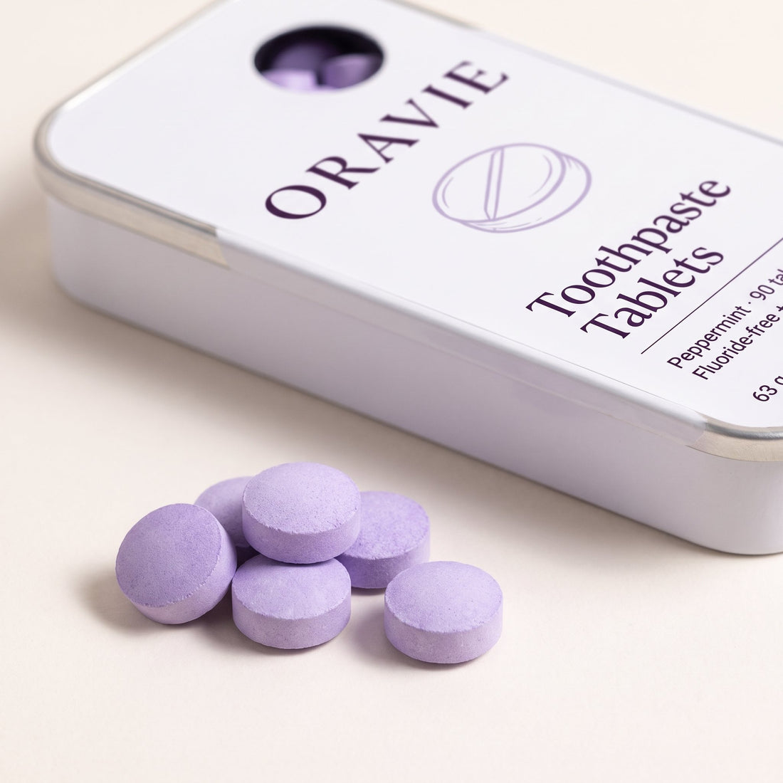 Close-up of round lavender toothpaste tablets in front of the ORAVIE tin