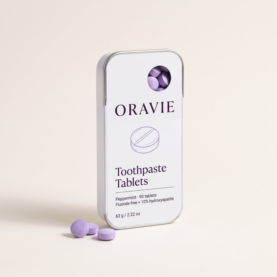 ORAVIE Toothpaste Tablets: slim white sliding tin of 90 peppermint tablets, with three lavender tablets beside it