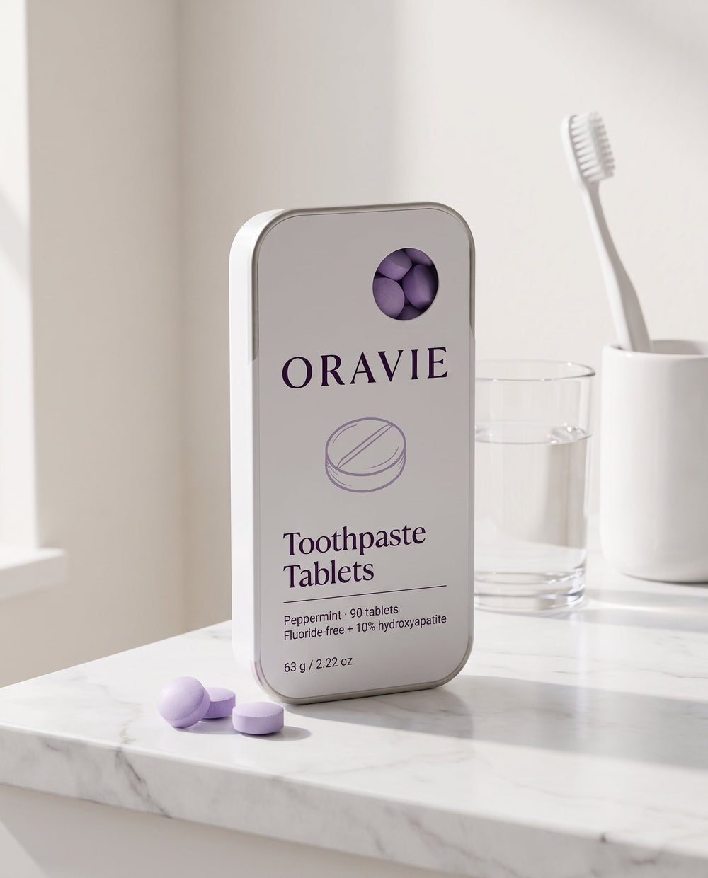 ORAVIE tin, a glass of water and a toothbrush on a marble bathroom counter